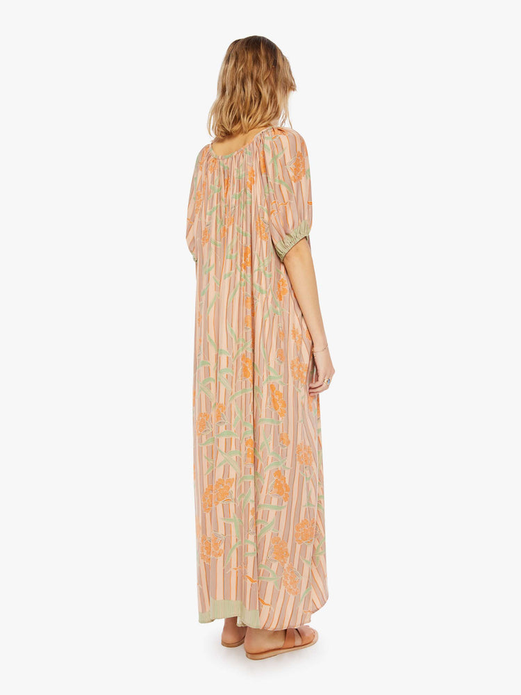 back  view of a woman in a cream maxi dress with stripes and a warm-toned floral print, designed with a scoop neck, elbow-length sleeves and an A-line cut for a loose, breezy feel.
