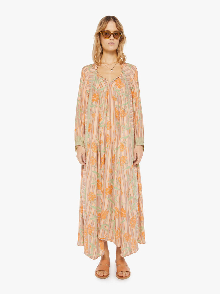 Front view of a woman in a cream dress with stripes and a warm-toned floral print. This maxi dress is designed with voluminous sleeves and has an A-line cut for a loose, breezy feel.
