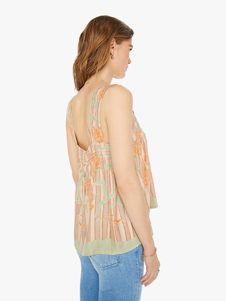 Back view of a woman in cream top with stripes and a warm-toned floral print, and features detailed straps and buttons in the back.