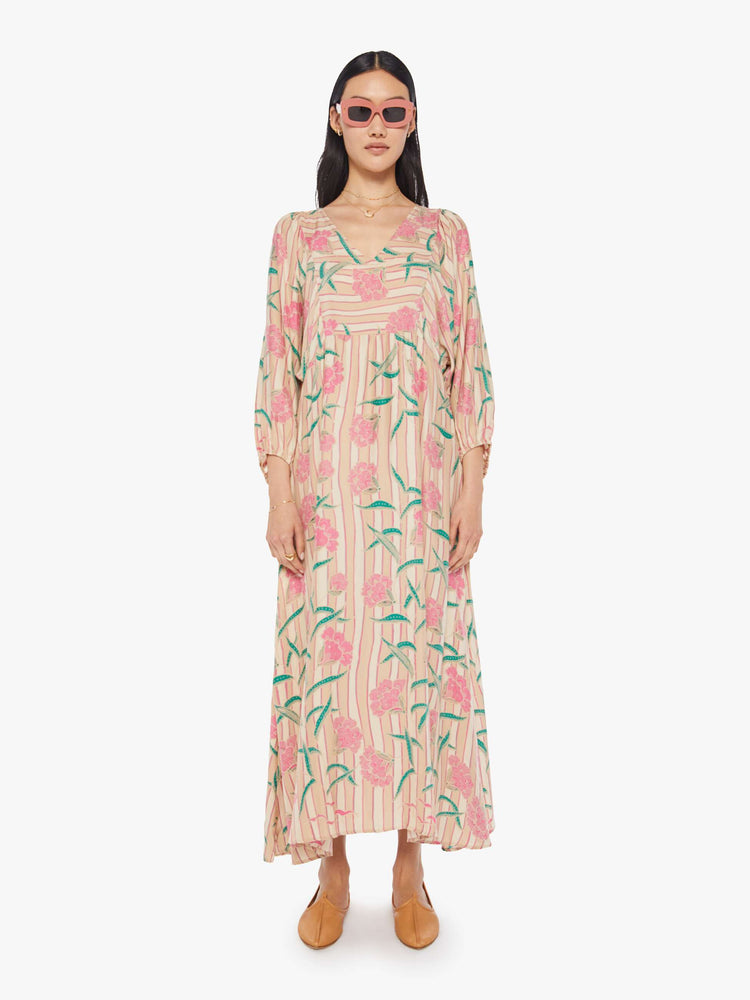 front view of a woman in a baby pink floral print maxi dress that is designed with a V-neck, long voluminous sleeves and has an A-line cut.