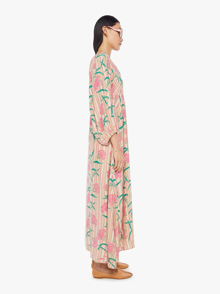 side view of a woman in a baby pink floral print maxi dress that is designed with a V-neck, long voluminous sleeves and has an A-line cut.