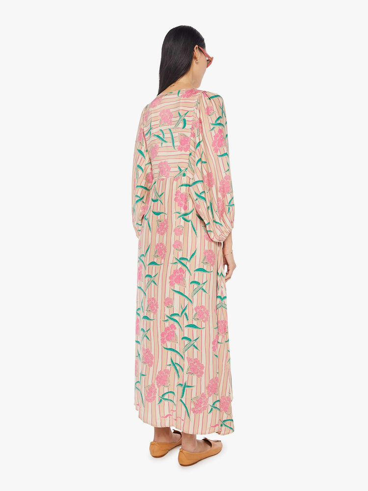 back view of a woman in a baby pink floral print maxi dress that is designed with a V-neck, long voluminous sleeves and has an A-line cut.