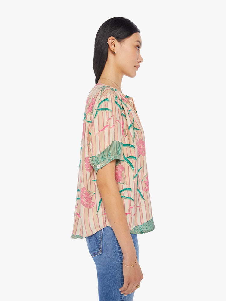 side view of a woman in a cream top with stripes and a baby pink floral print, the Violet top is designed with a deep V-neck, buttons down the front, short balloon sleeves and ruffles throughout for a loose, flowy fit.
