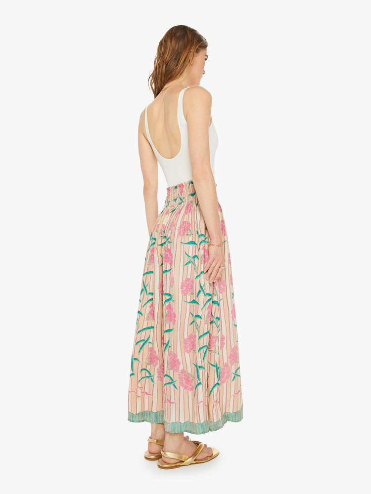 Back view of a woman in a n cream with stripes and a baby pink floral print, and features a smocked waistband and a loose, flowy fit maxi skirt.