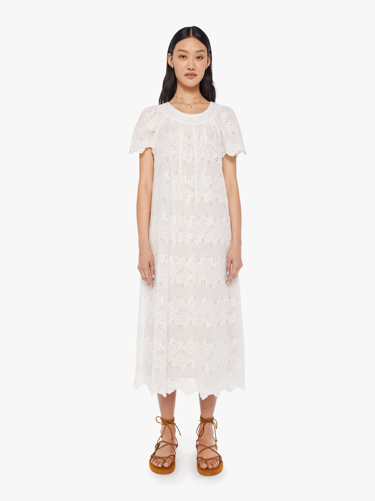 front view of a woman in a cream dress with eyelet details. The maxi dress is designed with a scoop neck, short flowy sleeves, a loose fit and a slip underneath.