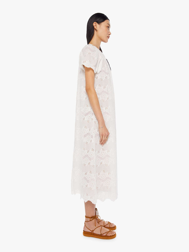 side view of a woman in a cream dress with eyelet details. The maxi dress is designed with a scoop neck, short flowy sleeves, a loose fit and a slip underneath.