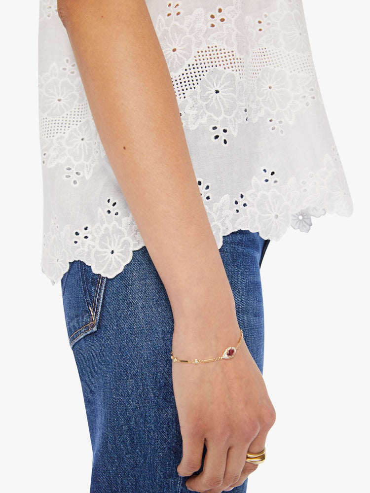 close-up view of a woman in a cream top with an eyelet floral print and a scalloped hem, designed with a deep V-neck, buttons down the front, short balloon sleeves and ruffles throughout for a loose, flowy fit.
