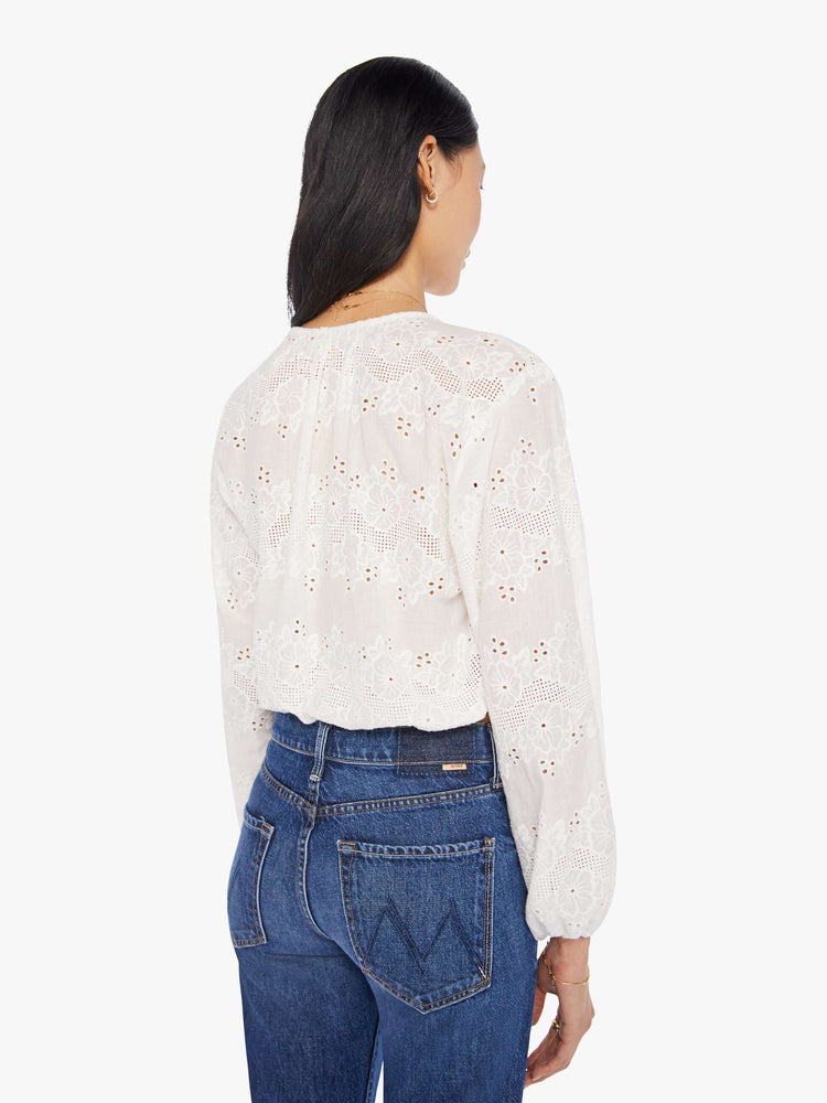back view of a woman in a cream top with an eyelet floral print, featuring a keyhole neckline with a tasseled tie closure, drop shoulders, long balloon sleeves and a cropped elastic hem.