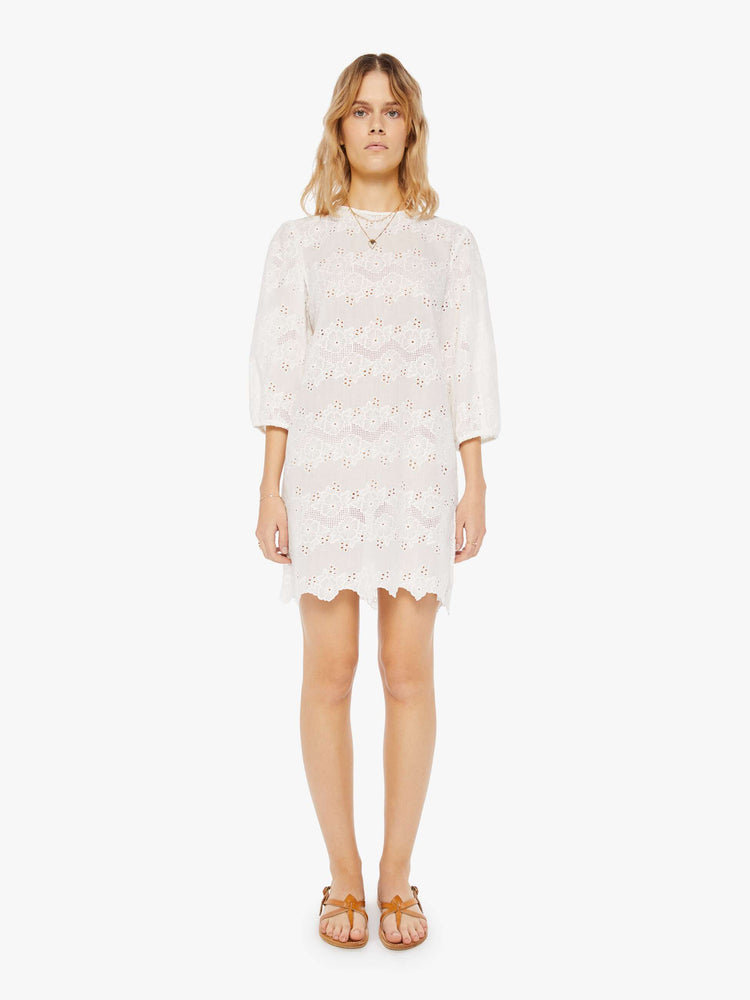 front view of a woman in a cream dress with eyelet details. The mini dress features a crewneck, 3/4-length sleeves, a loose fit and zig-zag hems.