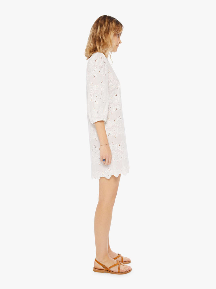 side view of a woman in a cream dress with eyelet details. The mini dress features a crewneck, 3/4-length sleeves, a loose fit and zig-zag hems.