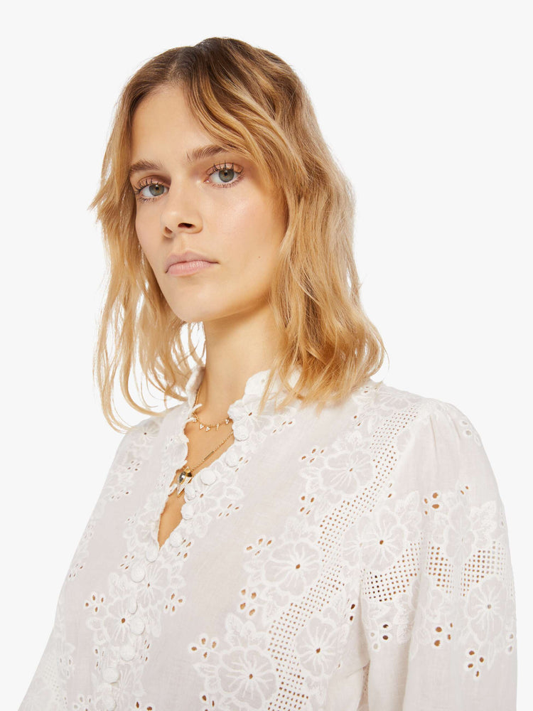 close up/swatch view of a woman in a cream dress with openwork details. The mini dress features a crewneck with a short collar, long flowy sleeves, a fitted waist and zig-zag hems.