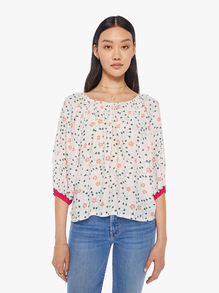front view of a woman in an off-white top with a colorful floral print and features an elastic boat neck that can be worn off-the-shoulder, 3/4-length balloon sleeves and a flowy fit.