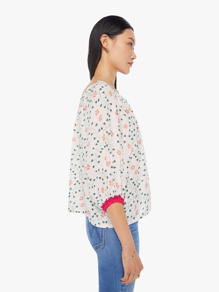 side view of a woman in an off-white top with a colorful floral print and features an elastic boat neck that can be worn off-the-shoulder, 3/4-length balloon sleeves and a flowy fit.