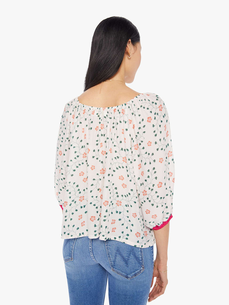 back view of a woman in an off-white top with a colorful floral print and features an elastic boat neck that can be worn off-the-shoulder, 3/4-length balloon sleeves and a flowy fit.