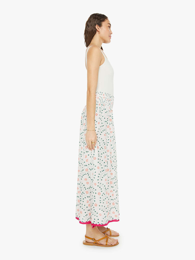 Side  view of a woman in a off-white with a colorful floral print, and features a smocked waistband and a loose, flowy fit maxi skirt.