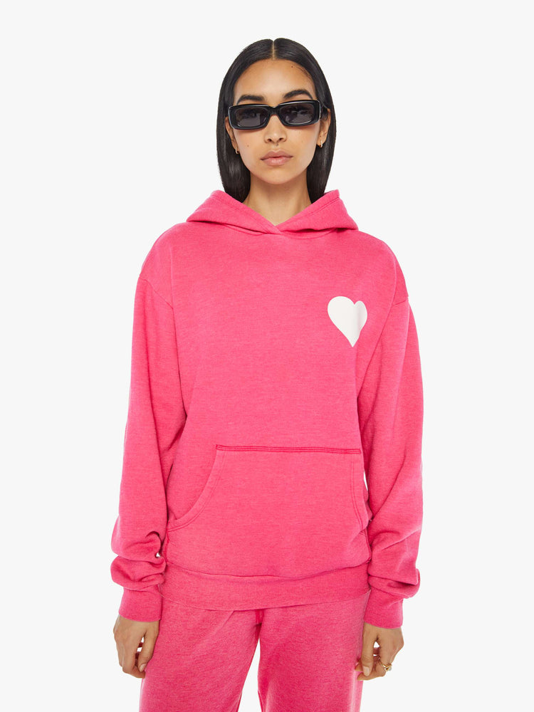 Front view of a womens hot pink sweatshirt hoodie featuring a front pocket and a white heart graphic.