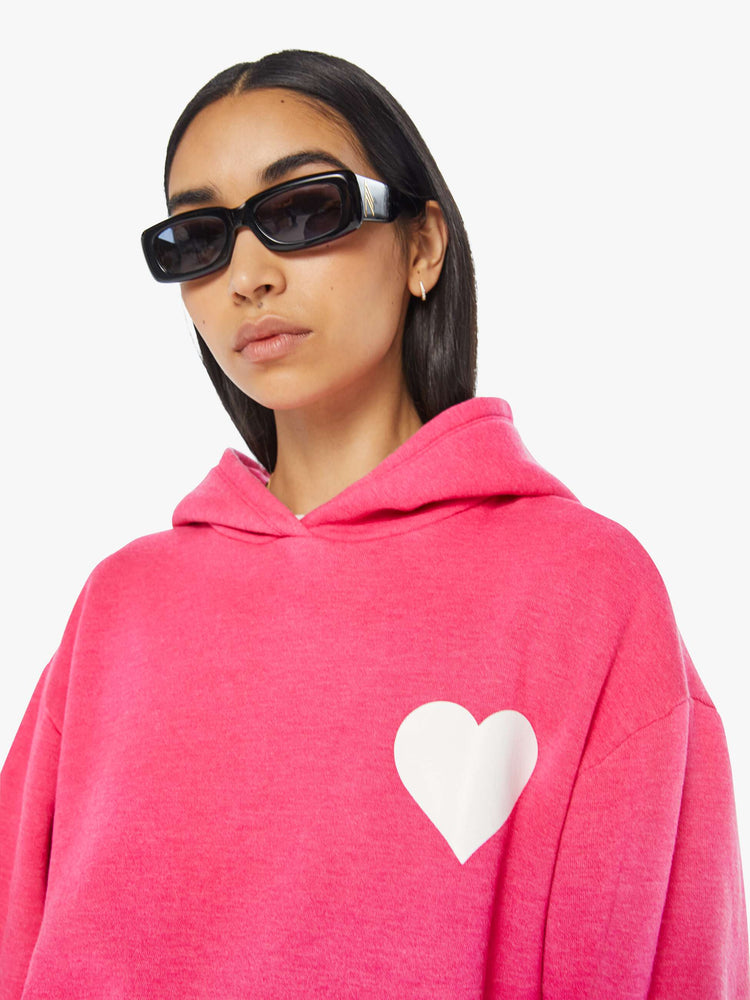 Front close up view of a womens hot pink sweatshirt hoodie featuring a front pocket and a white heart graphic.