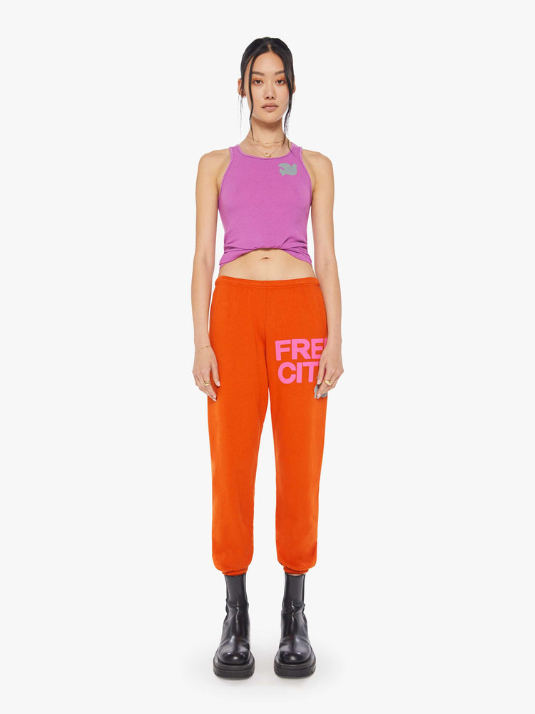 Front view of a woman wearing neon orange sweatpants and a bright purple tank.
