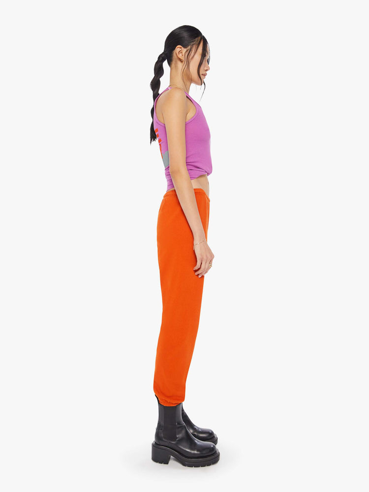 Side view of a woman wearing neon orange sweatpants and a bright purple tank.