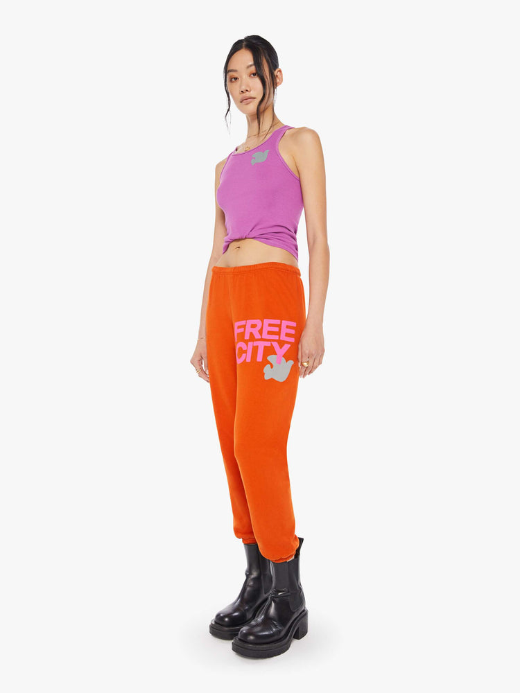 Front side view of a woman wearing neon orange sweatpants and a bright purple tank.