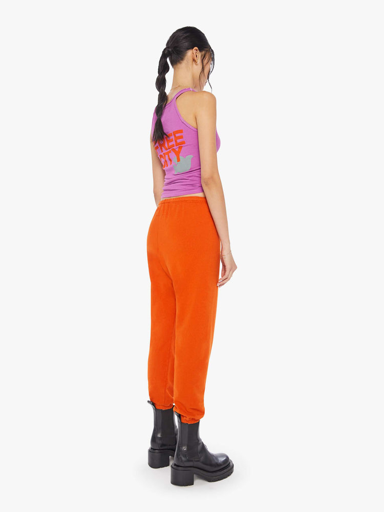 Back view of a woman wearing neon orange sweatpants and a bright purple tank.
