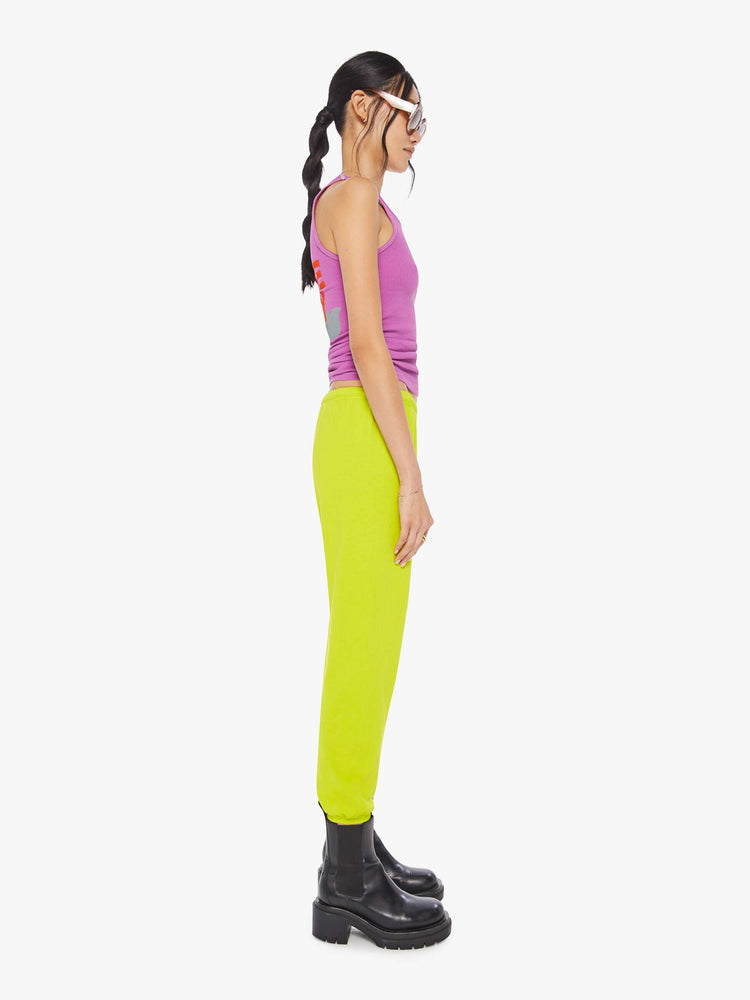 Side view of a woman wearing neon yellow sweatpants and a bright purple tank.
