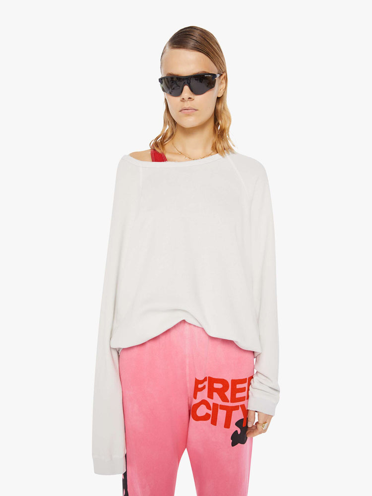 A front view of a woman wearing an oversized off white sweatshirt featuring raglan sleeves, paired with a bright pink sweatpant.
