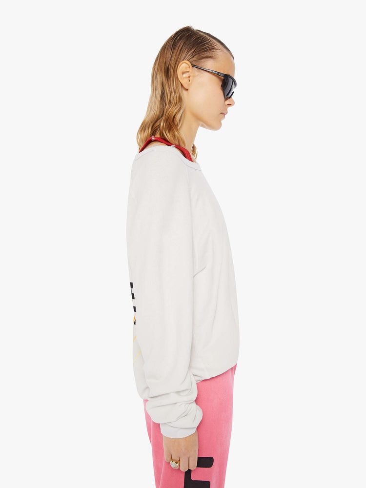 A side view of a woman wearing an oversized off white sweatshirt featuring a large back graphic, paired with a bright pink sweatpant.