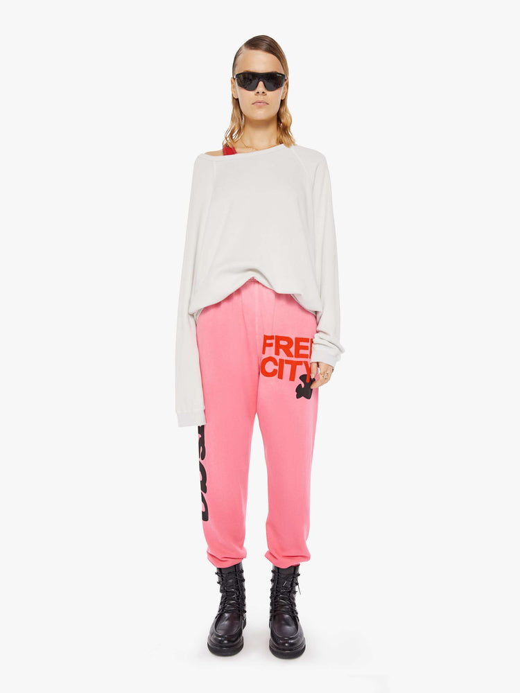 A front full body view of a woman wearing an oversized off white sweatshirt featuring raglan sleeves, paired with a bright pink sweatpant.