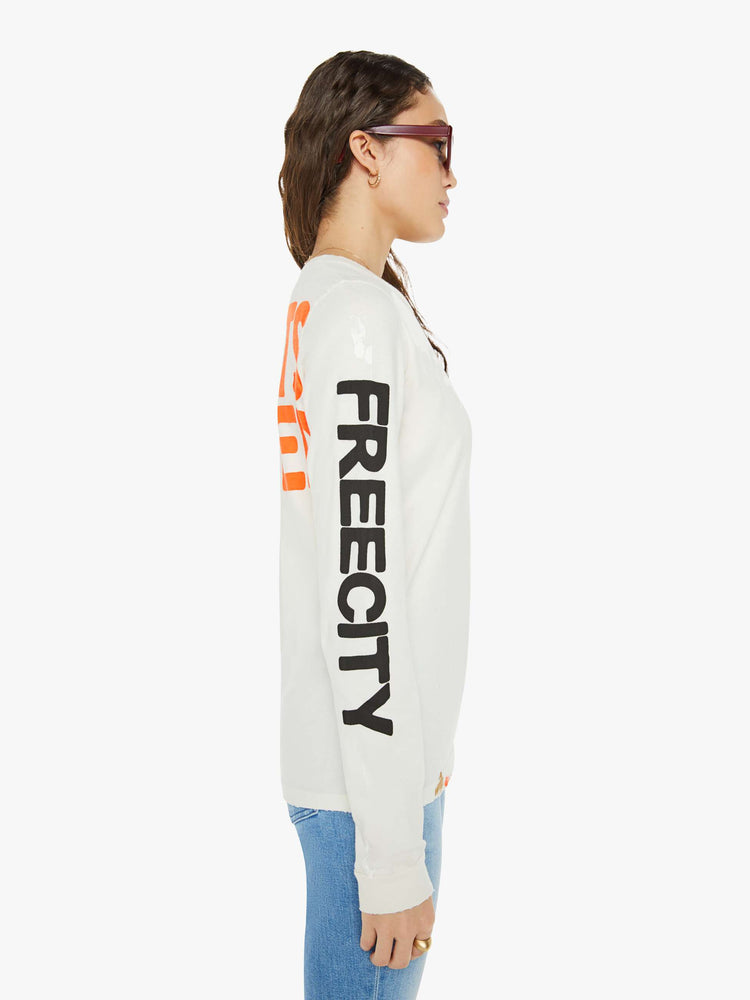 Side view of a woman in a white long sleeve with a crewneck, oversized fit, the brand's logo down the arms and a text graphic on the back.