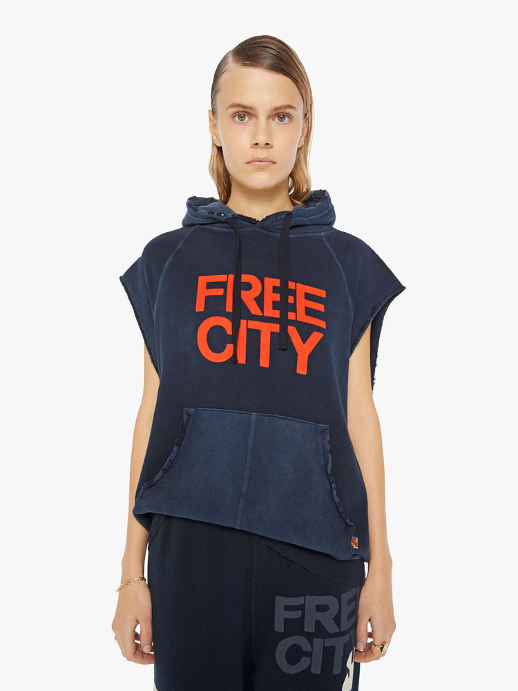A front view of a woman wearing an oversized navy sweatshirt hoodie with raw cutoff sleeves and a large front graphic reading "FREE CITY", paired with a dark navy sweatpant.
