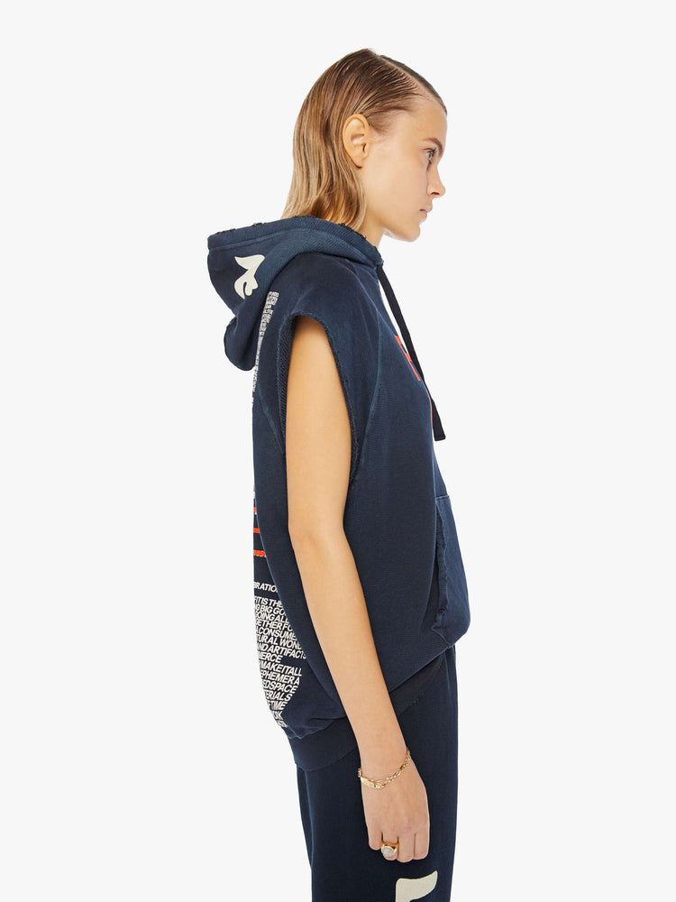 A side view of a woman wearing an oversized navy sweatshirt hoodie with raw cutoff sleeves and a large front graphic reading "FREE CITY", paired with a dark navy sweatpant.
