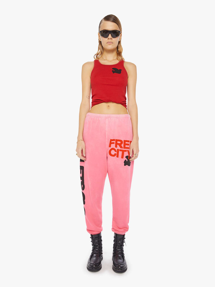 A front view of a woman wearing a bright pink sweatpant with graphics, paired with a bright red ribbed tank top.