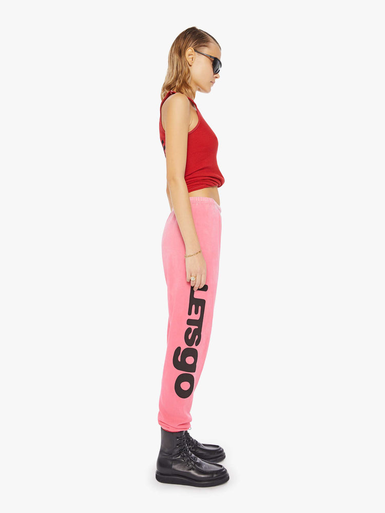 A Side view of a woman wearing a bright pink sweatpant with graphics, paired with a bright red ribbed tank top.