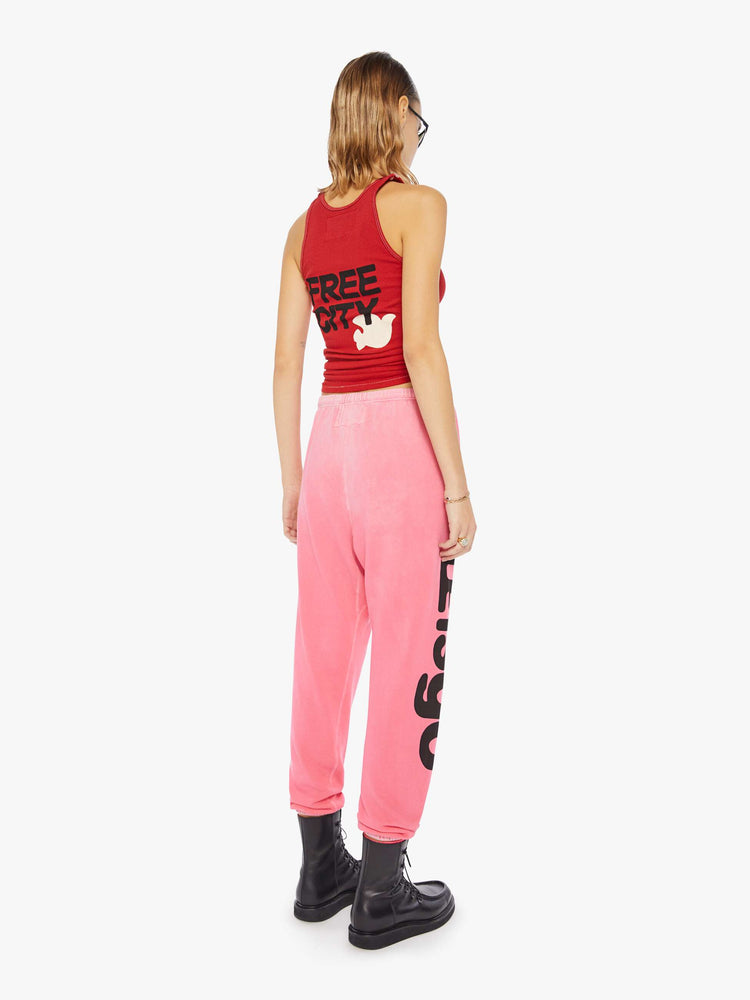 A back view of a woman wearing a bright pink sweatpant with graphics, paired with a bright red ribbed tank top.