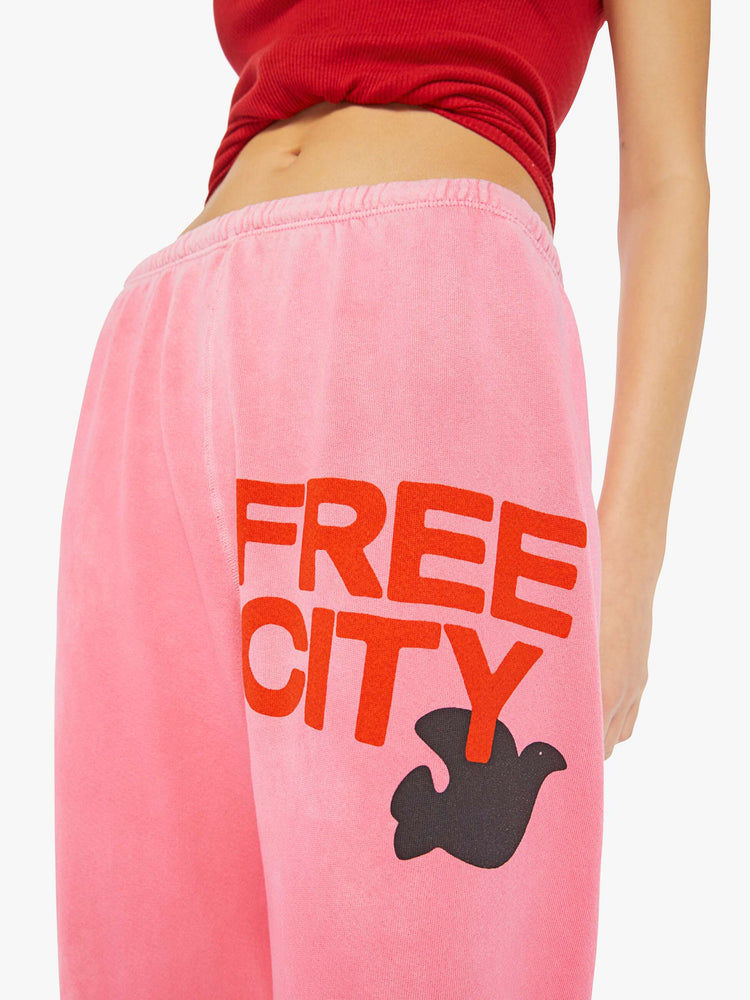 A front close up view of a woman wearing a bright pink sweatpant with graphics, paired with a bright red ribbed tank top.