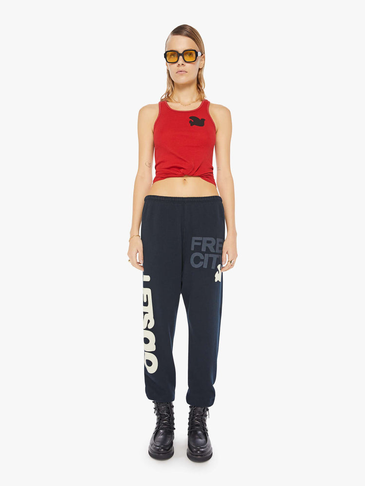 A front view of a woman wearing a bright red ribbed tank top with a bird graphic on the chest, paired with a dark navy sweatpants.