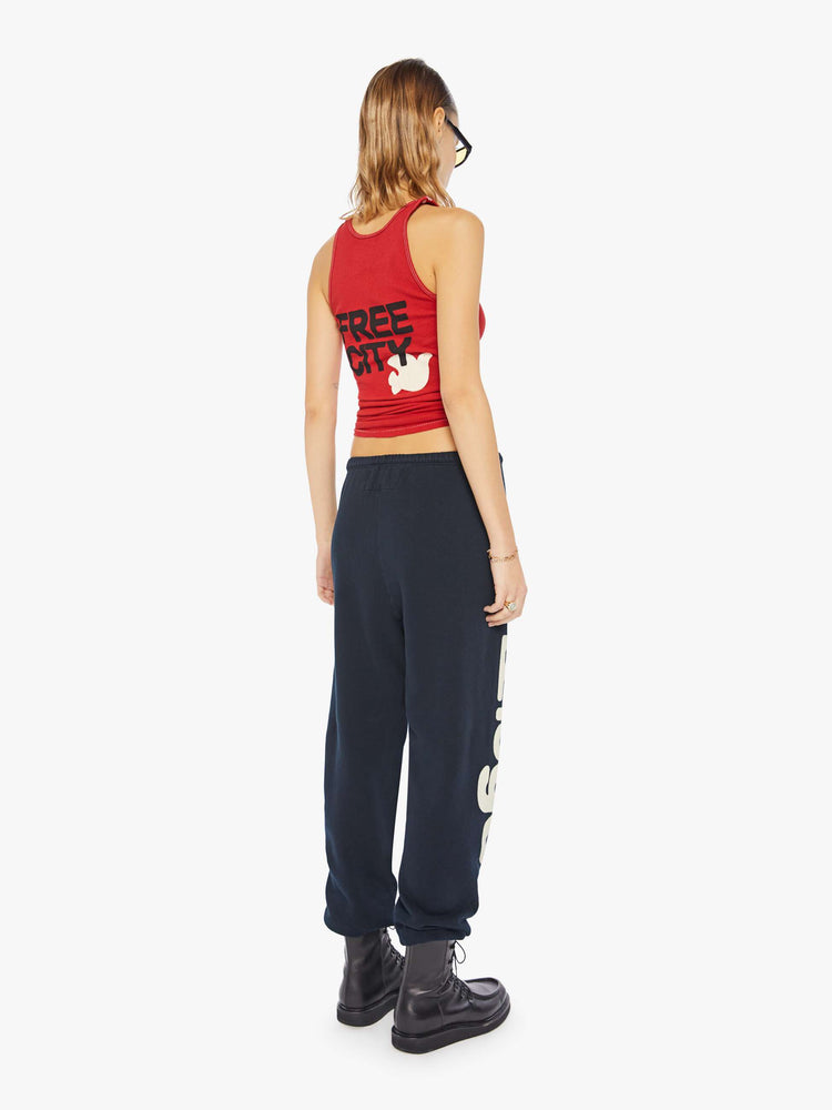 A back view of a woman wearing a bright red ribbed tank top with a bird graphic on the chest, paired with a dark navy sweatpants.