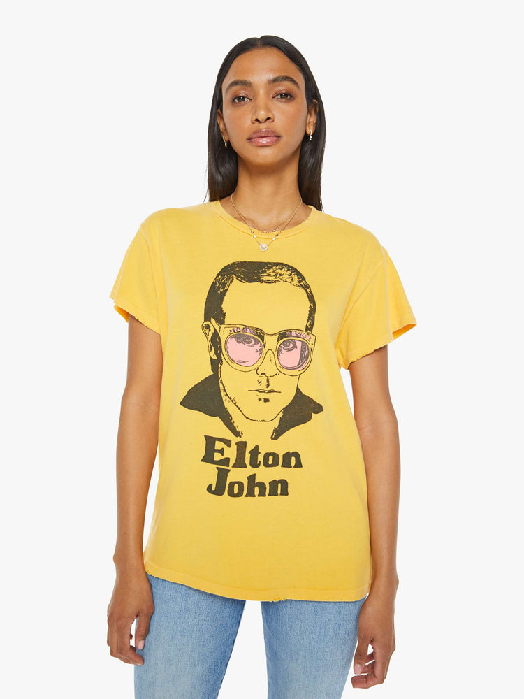 Front view of woman in a yellow tee in golden-yellow, the tee honors Elton John with a graphic portrait on the front.
