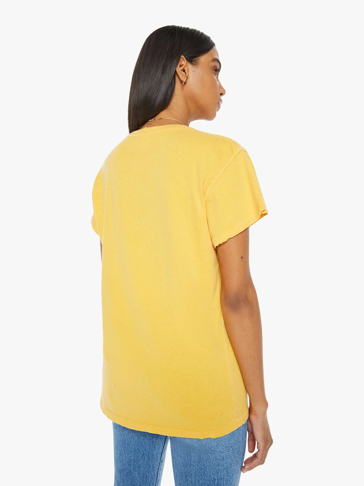 Back view of woman in a yellow tee in golden-yellow, the tee honors Elton John with a graphic portrait on the front.