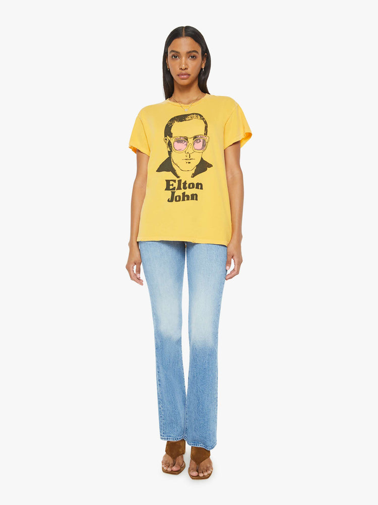 Full body view of woman in a yellow tee in golden-yellow, the tee honors Elton John with a graphic portrait on the front.