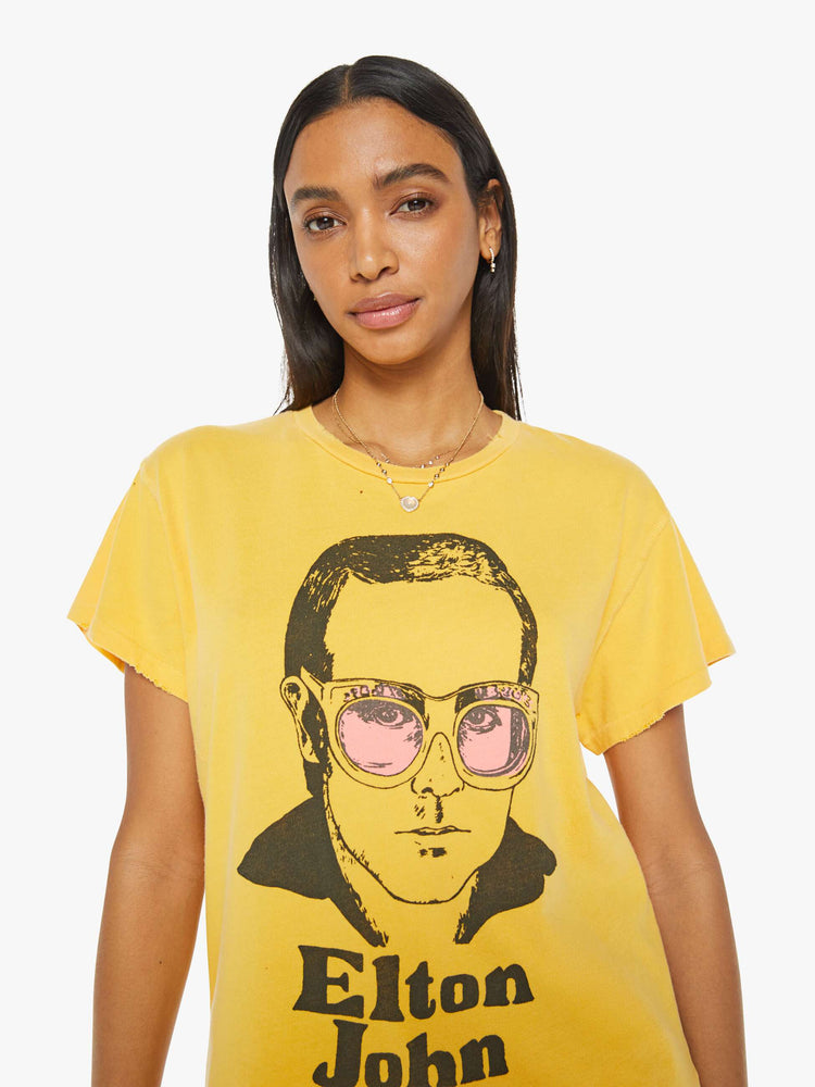 Close up view of woman in a yellow tee in golden-yellow, the tee honors Elton John with a graphic portrait on the front.