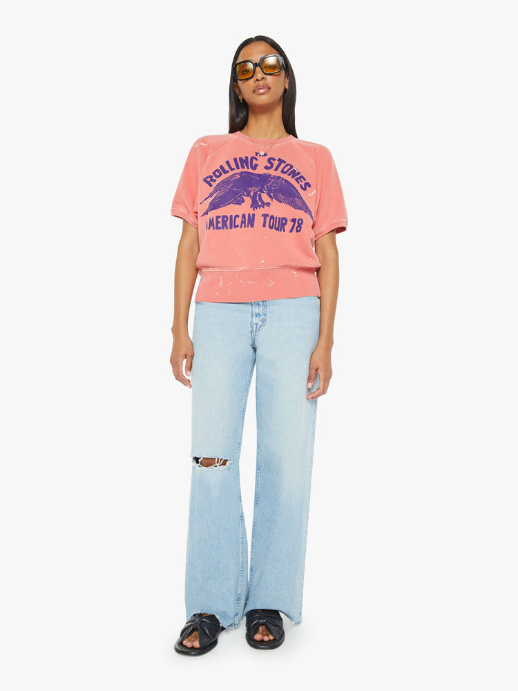 Full body view of a woman short sleeve sweatshirt in red, the sweatshirt pays homage to The Rolling Stones' 1978 tour with a faded text graphic in navy on the front.