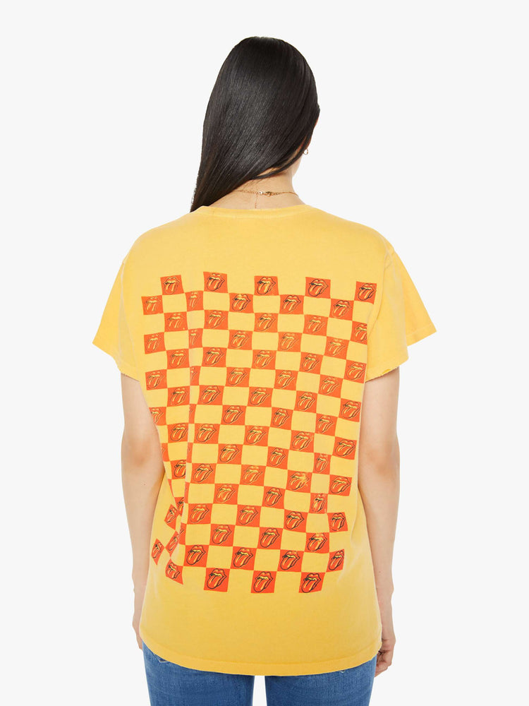 Back view of a woman tee in golden-yellow, the tee honors the Rolling Stones with the band's iconic tongue-and-lips logo on the front and a checker-print graphic on the back.