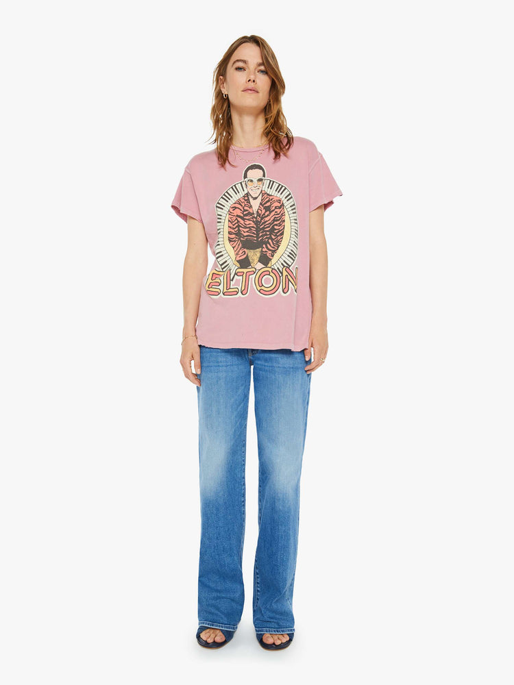 Full body view of a woman tee that pays homage to the British musician, Elton John, with bold text and a graphic portrait on the front.