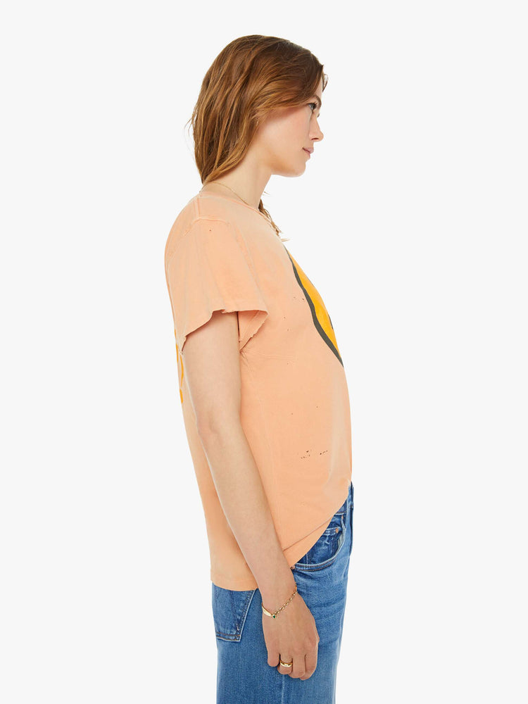 Side view of a woman peach tee with a smiley face graphic on the front and text on the back.