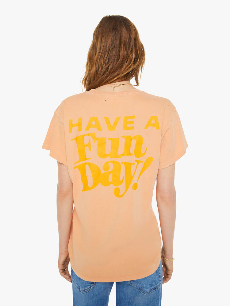 Back view of a woman peach tee with a smiley face graphic on the front and text on the back.