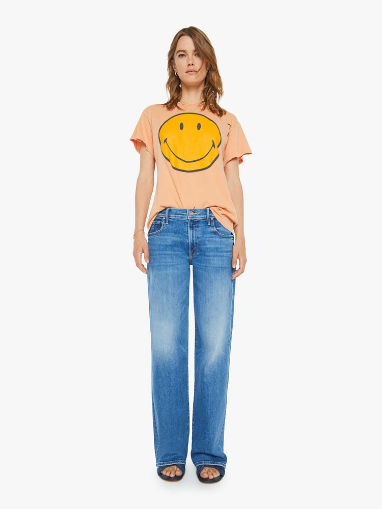 Full body view of a woman peach tee with a smiley face graphic on the front and text on the back.