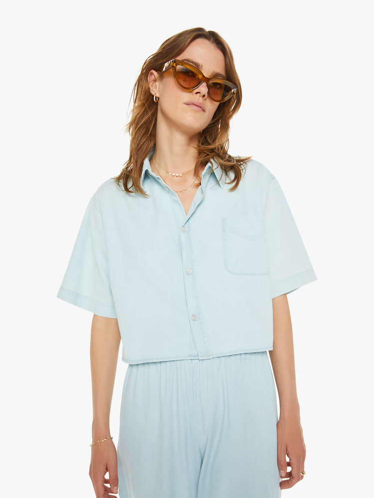 Front view of a woman sky blue button-up blouse with a patch pocket,  drop shoulders and a cropped, boxy fit. 