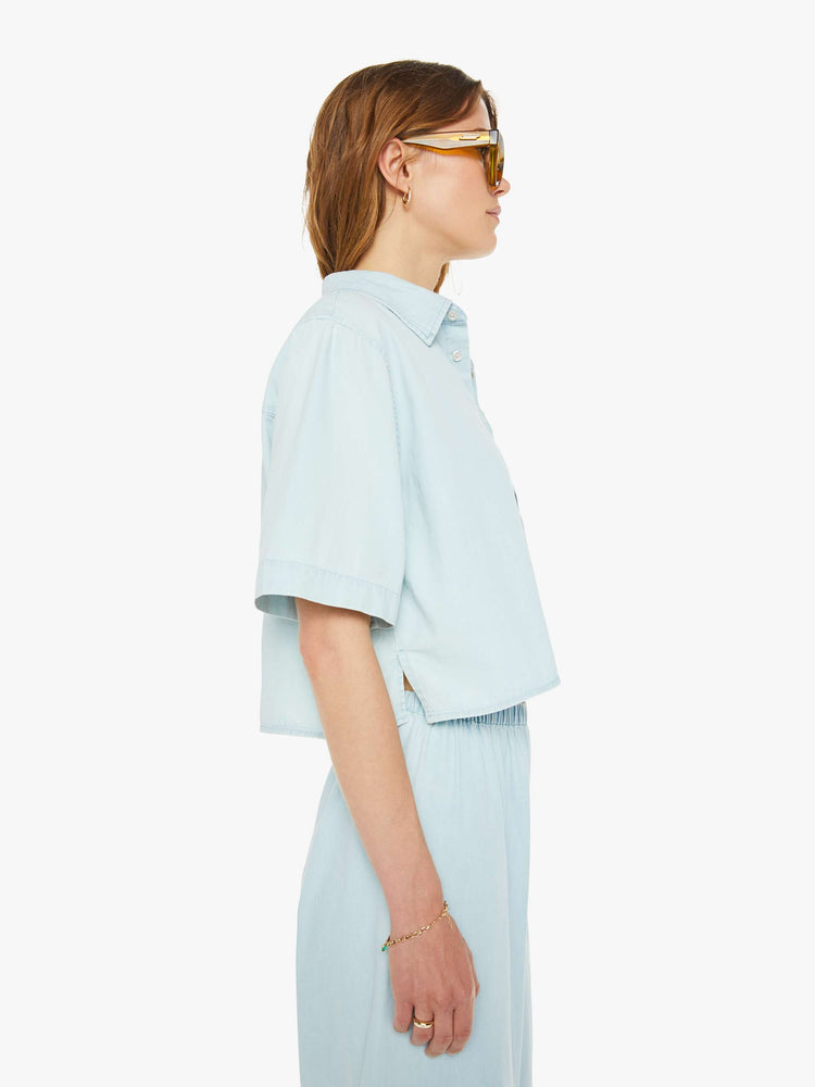 Side  view of a woman sky blue button-up blouse with a patch pocket, drop shoulders and a cropped, boxy fit.